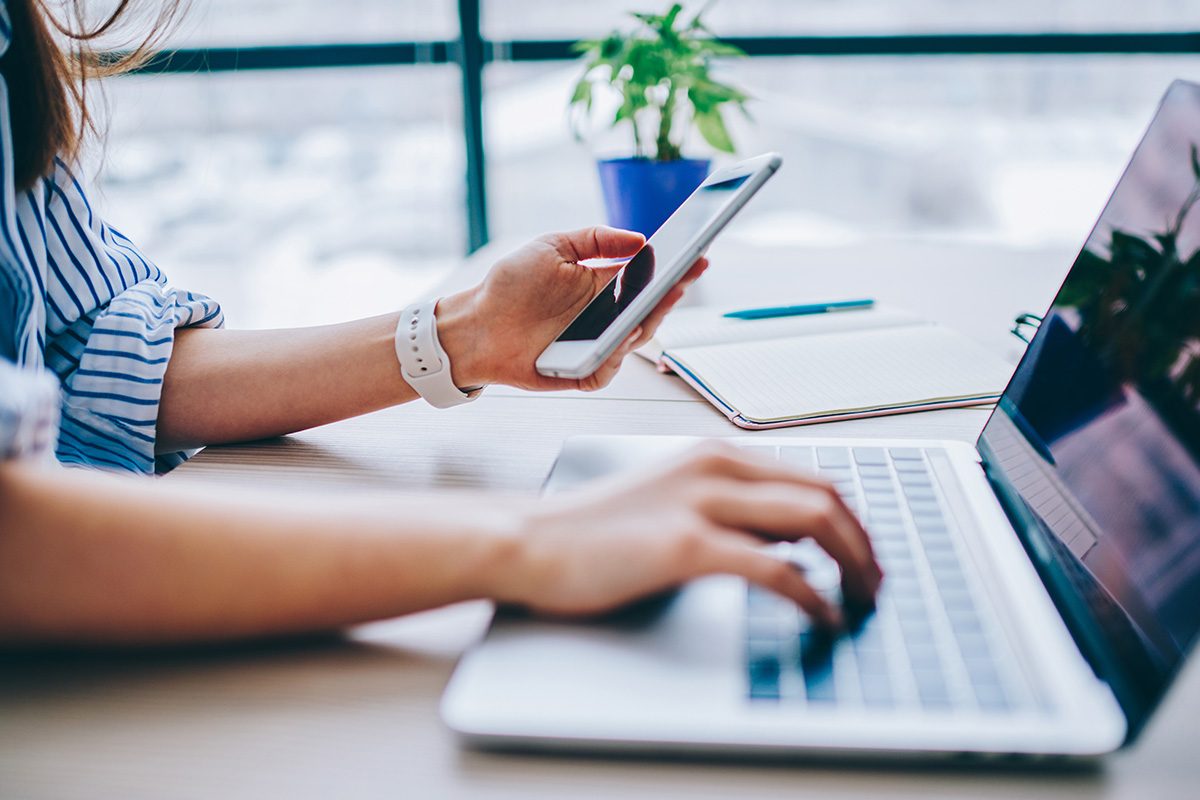 Frauenhände am Smartphone und am Laptop um Kontakt aufzunehmen