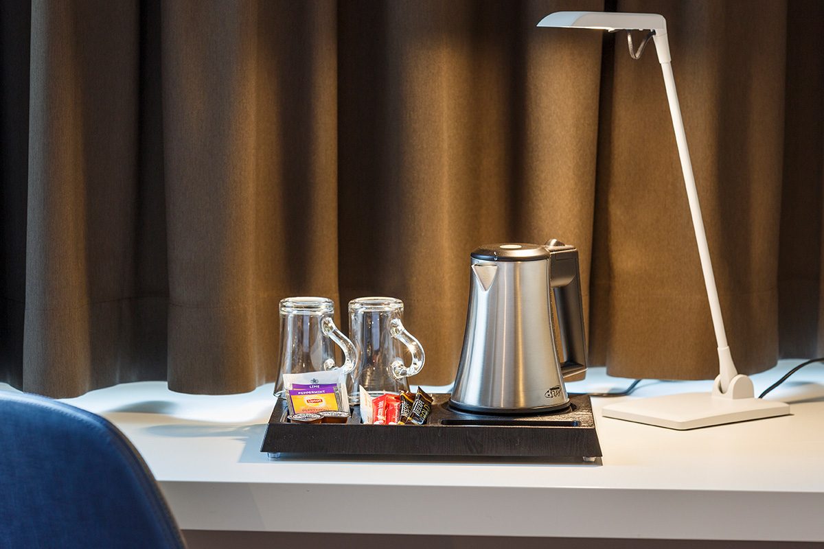 Wasserkocher mit Kaffee- und Tee Utensilien auf einem Tablett auf dem Schreibtisch neben einer Lampe