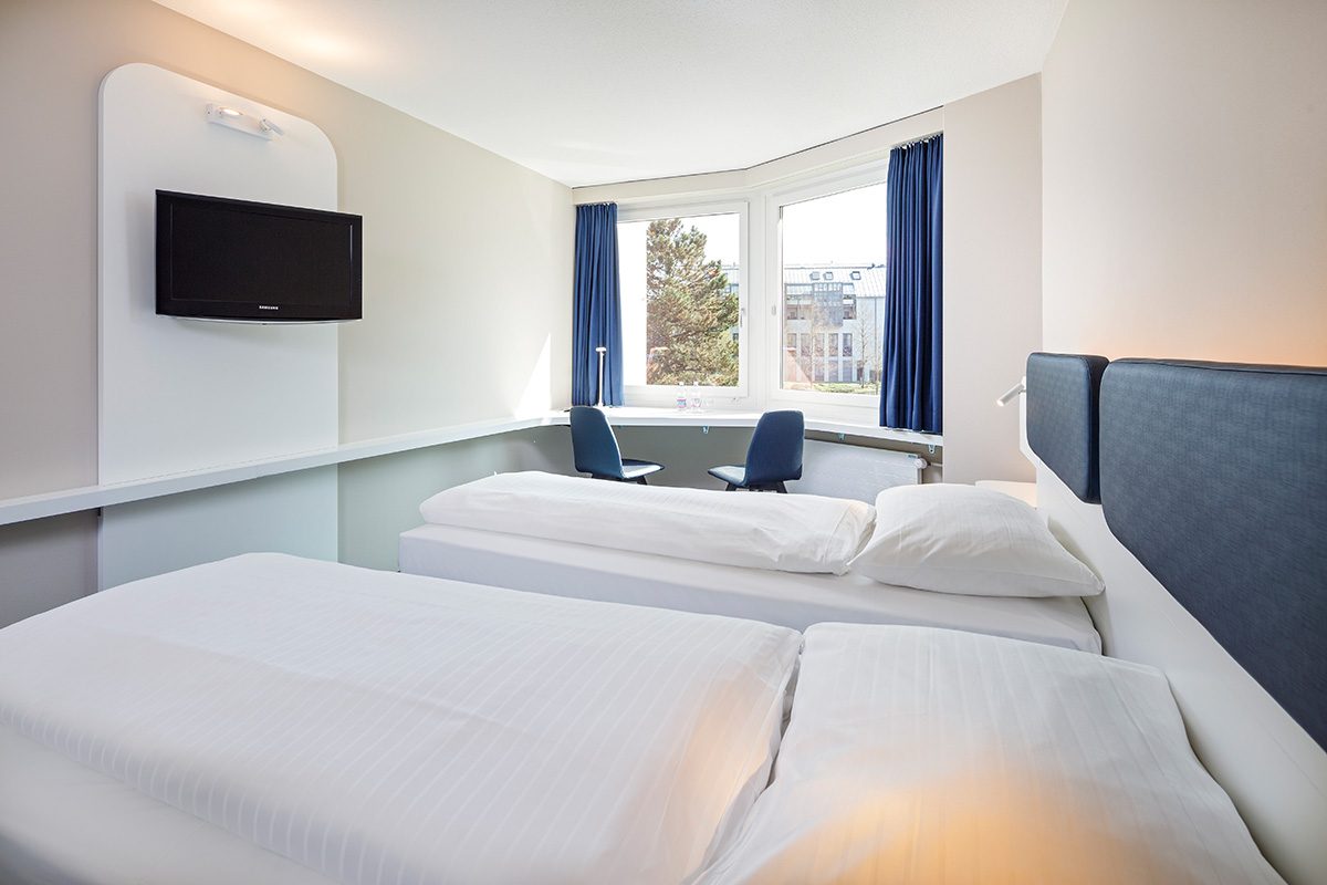 Zimmer mit zwei Betten, Sitzgelegenheiten und Fernseher an der Wand